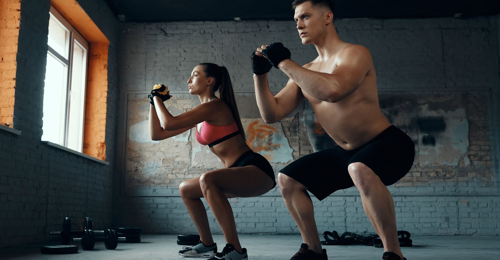 Confident fit couple standing in squatting position while exercising in gym together